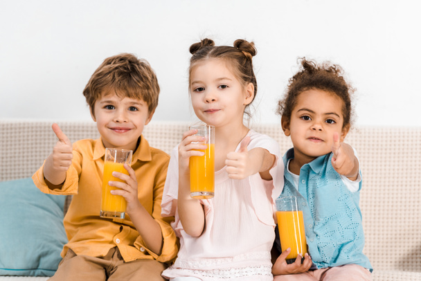χαριτωμένα παιδιά πολυεθνική κρατώντας ποτήρια χυμό και δείχνει τους αντίχειρες επάνω  - Φωτογραφία, εικόνα
