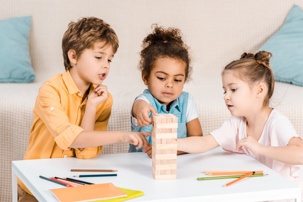 cute focused children building tower from wooden blocks on table - Fotó, kép