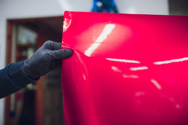 Car wrapping specialist putting vinyl foil or film on car wrapping protective film yacht, boat, ship, car, mobile home. pink red film hand pulls - Φωτογραφία, εικόνα