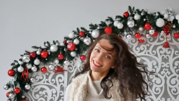 Die schöne lockige Brünette schüttelt ihre Haare und lacht vor der Kamera über den Hintergrund der Weihnachtsdekoration. attraktive brünette weiblich, indoor shot - Filmmaterial, Video