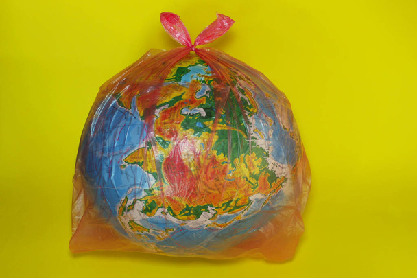 Streszczenie tło. Całym świecie w plastikowej torbie na żółtym tle. Problemy środowiskowe, zanieczyszczeń przyroda i ekologia koncepcja. - Zdjęcie, obraz