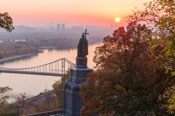 Saint Vladimir Monument, built in the mid 19th century against the backdrop of the Dnieper River, city building and rising sun at autumn, Kiev, Ukraine - Photo, Image