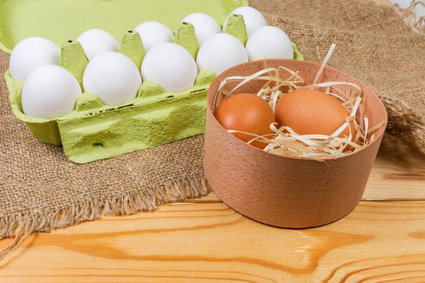 Oeufs de poulet brun dans une boîte ronde en bois sur fond d'œufs blancs en carton ouvert en pâte à papier recyclé sur une table rustique avec sac au foyer sélectif
 - Photo, image