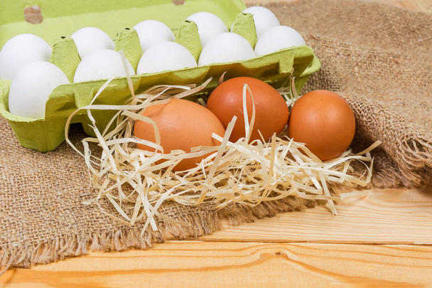 セレクティブ フォーカスで荒布の素朴なテーブルの上の白い卵と古紙パルプの卵のカートンの背景に茶色の鶏の卵します。 - 写真・画像