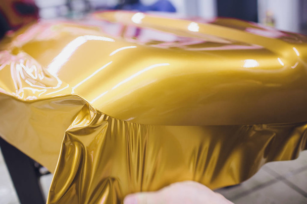 Car wrapping specialist putting vinyl foil or film on car wrapping protective film yacht, boat, ship, car, mobile home. yellow gold film hand pulls - Photo, image