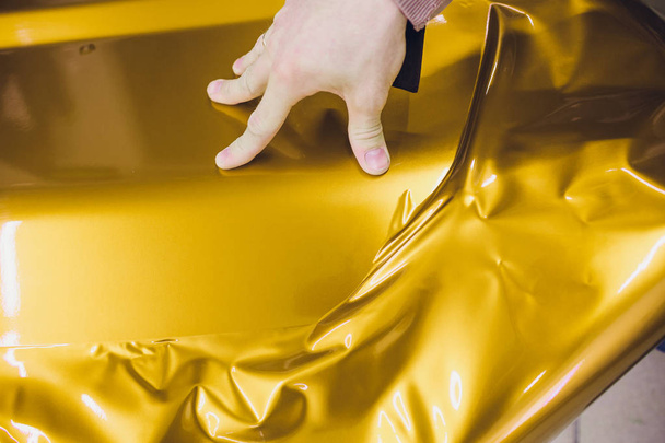 Car wrapping specialist putting vinyl foil or film on car wrapping protective film yacht, boat, ship, car, mobile home. yellow gold film hand pulls - Foto, imagen