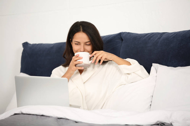 Jonge vrouw met laptop rusten op bed - Foto, afbeelding