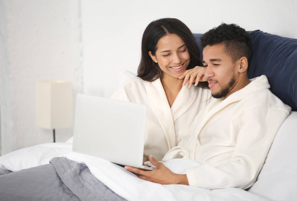 Young couple with laptop resting in bed - Φωτογραφία, εικόνα