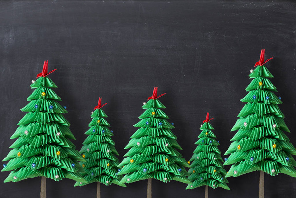 Origami-Weihnachtsbäume aus grünem Papier auf dunklem Hintergrund oder Tafel, mit Kopierraum - Foto, Bild