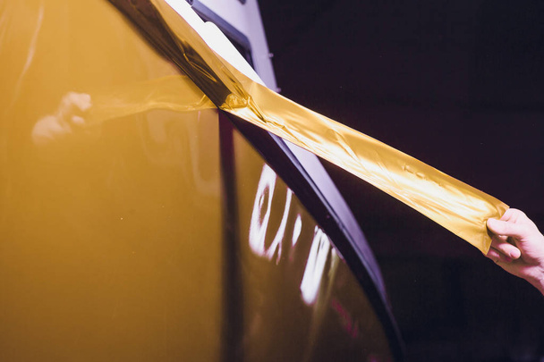 Αυτοκίνητο ειδικός αναδίπλωσης βάζοντας βινυλίου αλουμινόχαρτο ή μεμβράνη στο αυτοκίνητο περιτυλίγματος προστατευτικό φιλμ γιοτ, πλοίο, αυτοκίνητο, σκάφος, κινητό σπίτι. Κίτρινο χρυσό ταινία χέρι τραβά - Φωτογραφία, εικόνα