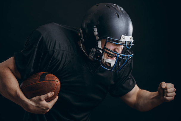 American football sportsman player in action isolated over black studio wall - Foto, afbeelding