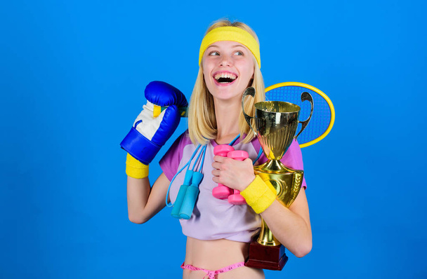 Girl successful modern woman hold golden goblet of sport champion and equipment blue background. How to find time for everything. Sport equipment store. Sport for every day. Sport shop assortment - Fotó, kép