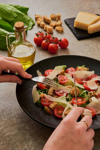 Caesar salad on a black plate, ingredients, hands - Фото, зображення