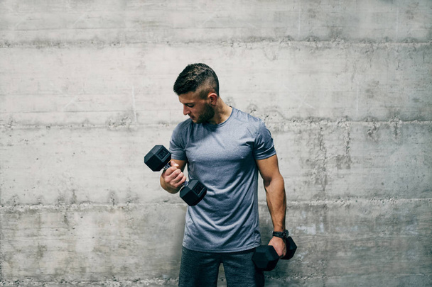 Man standing in front of wall and lifting dumbbells - Fotografie, Obrázek