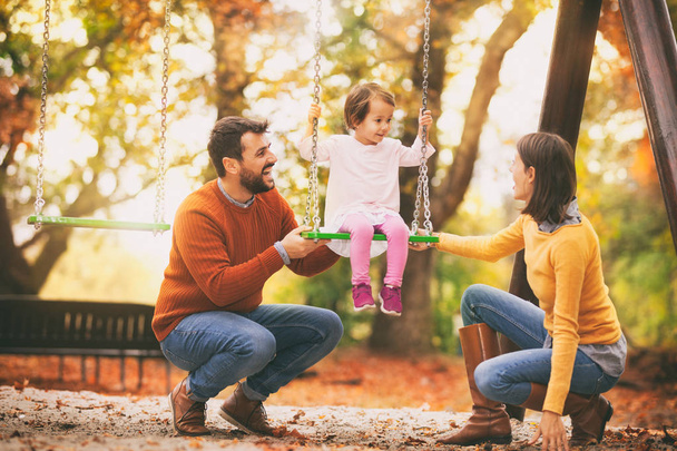 Sorrindo mãe e pai balançando menina no parque, família se divertir juntos
 - Foto, Imagem