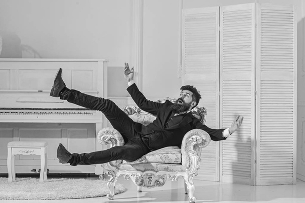 Fashion and style concept. Man with beard and mustache wearing fashionable classic suit, sits, jumps on old fashioned armchair. Macho attractive and elegant on shocked face and surprised expression - Foto, Imagem