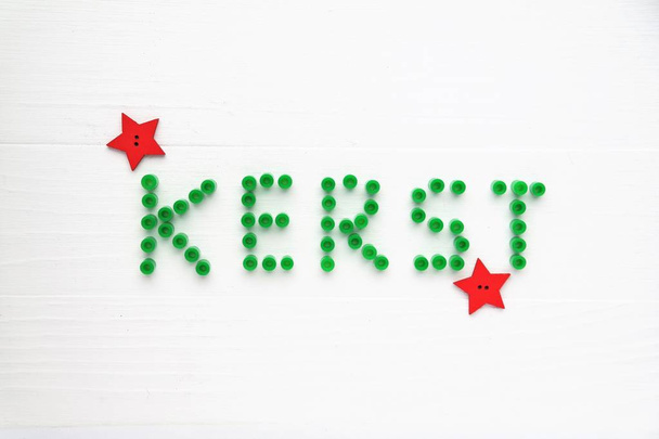 Kerstkaart in Nederlandse taal. Decoratieve groene letters en rode sterren. Witte houten achtergrond, bovenaanzicht perspectief en tekst ruimte.  - Foto, afbeelding