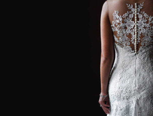 Rückseite der Frau im eleganten Hochzeitskleid mit Spitze auf schwarzem Hintergrund - Foto, Bild