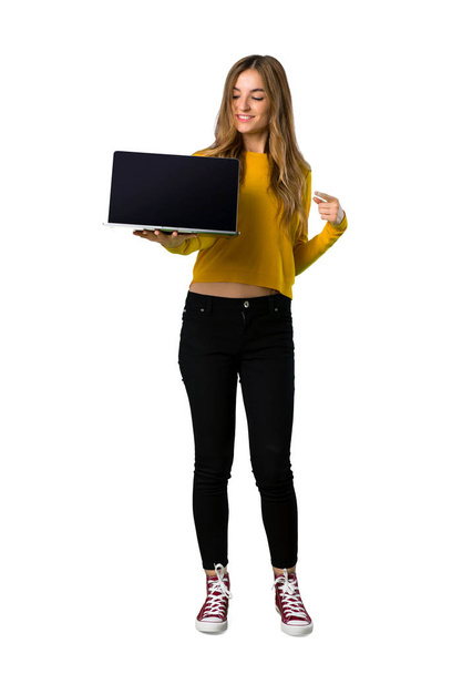 Un plan complet d'une jeune fille avec un pull jaune montrant un ordinateur portable sur fond blanc isolé
 - Photo, image
