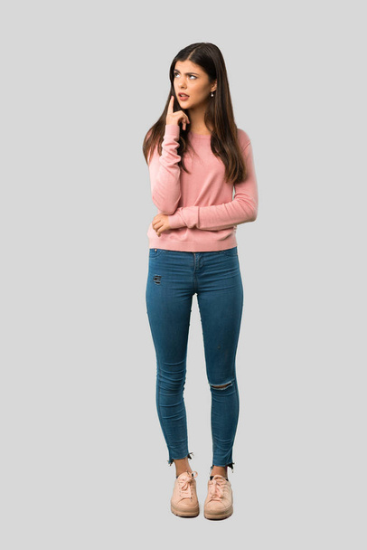 Full body of Teenager girl with pink shirt having doubts while looking up on isolated grey background - Фото, изображение
