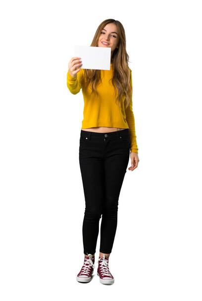Un plan complet d'une jeune fille avec un pull jaune tenant une pancarte blanche vide sur fond blanc isolé
 - Photo, image
