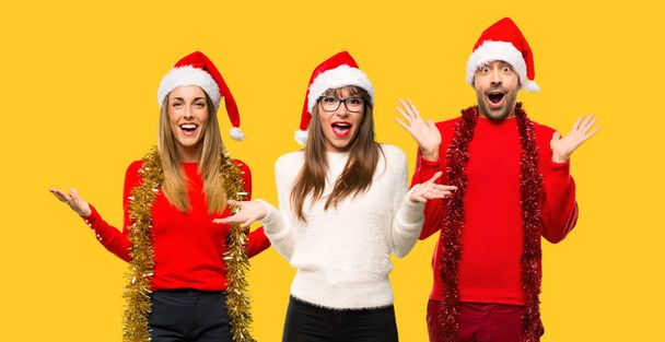 A group of people Blonde woman dressed up for christmas holidays with surprise expression because not expect what has happened on yellow background - Photo, Image
