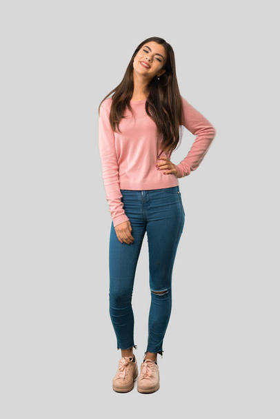 Повне тіло дівчини-підлітка з рожевою сорочкою позує з руками на стегні і посміхається на ізольованому сірому фоні
 - Фото, зображення