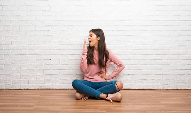 Menina adolescente sentada no chão em uma sala bocejando e cobrindo a boca aberta com a mão
 - Foto, Imagem