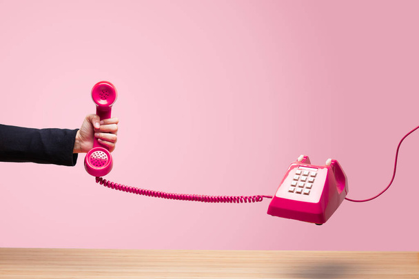 Mulher de negócios segurando o telefone vermelho, chamada urgente esperando, receptor de telefone vermelho clássico na mão vestindo terno preto, telefone antigo no fundo branco, voando em ausência de peso
. - Foto, Imagem
