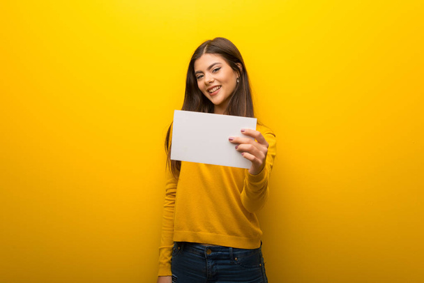 Menina adolescente no fundo amarelo vibrante segurando um cartaz branco vazio
 - Foto, Imagem