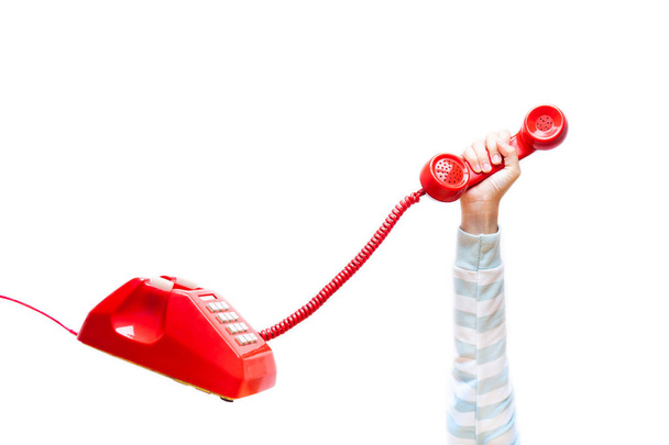 Ręka trzyma telefon, ramię noszenia sweter, klasyczna czerwona słuchawka, stary telefon na białym tle na białym tle pływające w nieważkości. Pojęcie Hot line, pomoc, obsługa klienta. - Zdjęcie, obraz