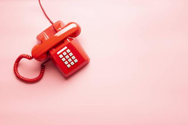 Vista superior del teléfono rojo sobre escritorio o fondo rosa, llamada telefónica de espera, timbre telefónico, vintage, teléfono rojo clásico
. - Foto, Imagen