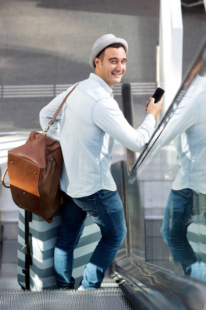 旅行スーツケース バッグと携帯電話でエスカレーターに男性の後ろから肖像画  - 写真・画像