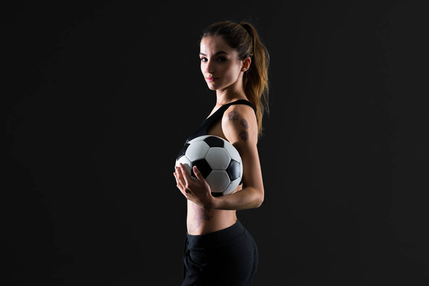 Αθλητισμός γυναίκα σε σκούρο φόντο, κρατώντας μια μπάλα ποδοσφαίρου - Φωτογραφία, εικόνα