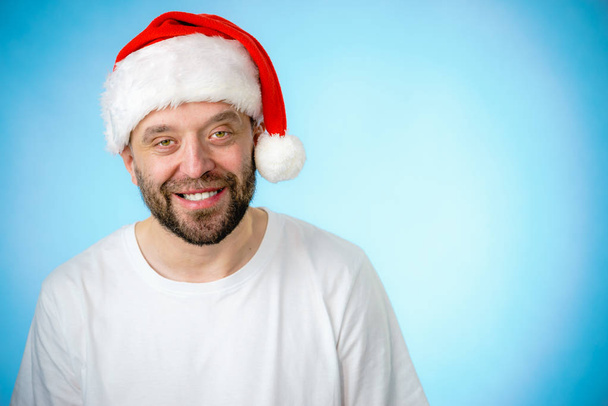 Bearded man wearing santa claus hat portrait, on blue with copy space. Christmas time. - 写真・画像