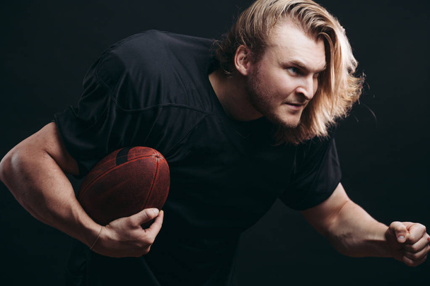 Determined American football player in action isolated on black background - Foto, Imagen