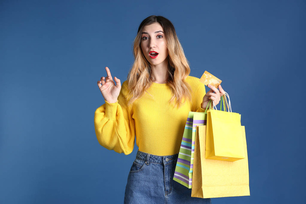 Beautiful young woman with shopping bags and credit card on color background - Foto, Imagem