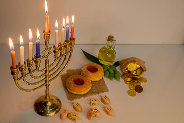 Εβραϊκή αργία εορτασμό hanukkah με menorah (παραδοσιακό μανουάλια), ξύλινο dreidels (σβούρα), ντόνατ, ελαιόλαδο και σοκολατένια νομίσματα σε λευκό τραπέζι. Πίνακας. Πίνακας. - Φωτογραφία, εικόνα