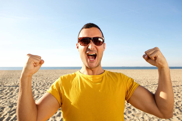 Close up portrait of cheerful man with hands raised at the beach - Photo, Image