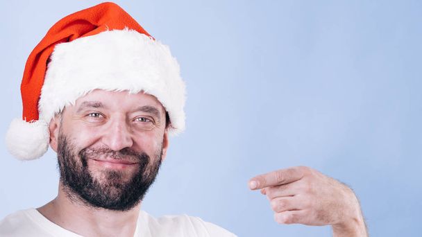 Christmas man wearing santa claus hat pointing with finger at you, on blue - Foto, Imagem