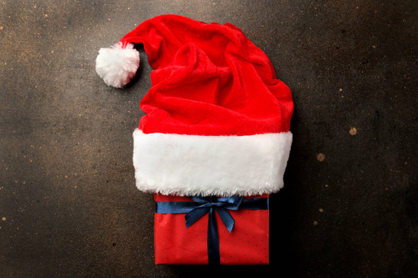 赤サンタ クロースの帽子と暗い茶色の背景にプレゼントを。クリスマス。新しい年. - 写真・画像