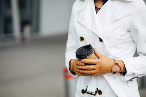 Портрет успешной деловой женщины, держащей чашку горячего напитка в руке по дороге на работу на городскую улицу. Красивая женщина с чашкой кофе возле офисного здания
. - Фото, изображение