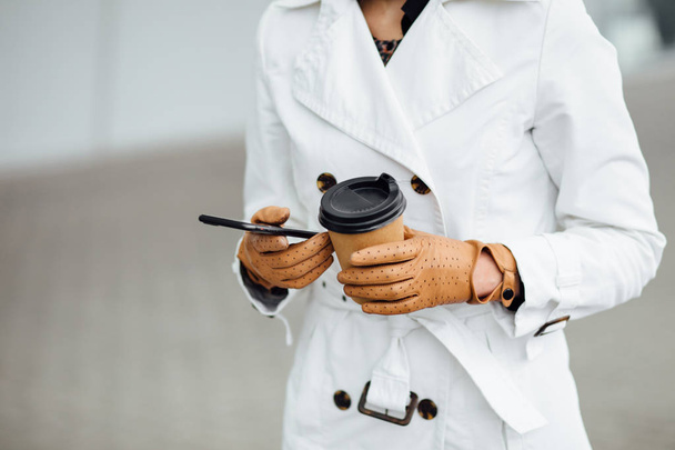 Portrait of successful business woman holding cup of hot drink in hand on her way to work on city street. Beautiful woman with coffee cup near office building. - Фото, изображение