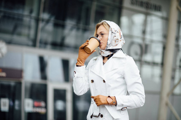 Portrait of successful business woman holding cup of hot drink in hand on her way to work on city street. Beautiful woman with coffee cup near office building. - Foto, Bild
