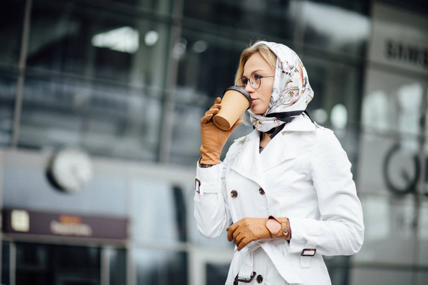 Portrait of successful business woman holding cup of hot drink in hand on her way to work on city street. Beautiful woman with coffee cup near office building. - Foto, Imagem