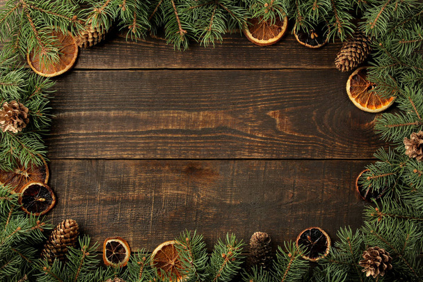 Χριστούγεννα και Πρωτοχρονιά πλαίσιο κειμένου με το χριστουγεννιάτικο δέντρο και κουκουνάρια και αποξηραμένα πορτοκάλια σε καφέ φόντο. θέα από ψηλά. - Φωτογραφία, εικόνα