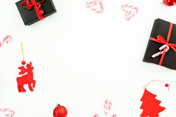 Composizione cornice invernale di Natale. Confezione regalo, decorazione rossa, bastoncini di zucchero e confetti su sfondo bianco. Posa piatta, vista dall'alto
. - Foto, immagini