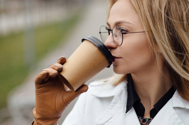 Portrait of successful business woman holding cup of hot drink in hand on her way to work on city street. Beautiful woman with coffee cup near office building. - Fotografie, Obrázek