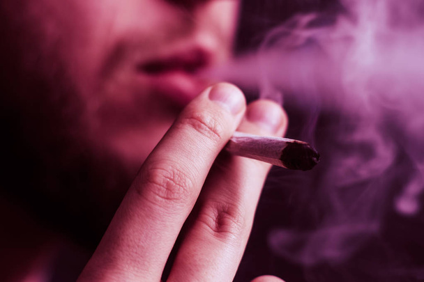 Концепции использования медицинской марихуаны и легализации марихуаны. Дым на черном фоне. Мужчина курит марихуану, косяк и зажигалку в руках. На черном фоне Вайолет тонировка
 - Фото, изображение