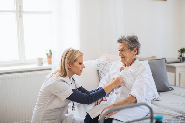 A health visitor helping a sick senior woman sitting on bed at home. - Фото, зображення